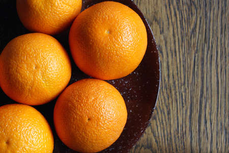 Orange oranges on a brown plate. The plate is made of clay and stands on a wooden surface. The apple is fresh and ready to eat.の写真素材