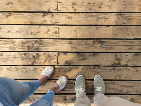 Two people are standing on a wooden surface. Top view of feet shod in light summer shoes.の写真素材