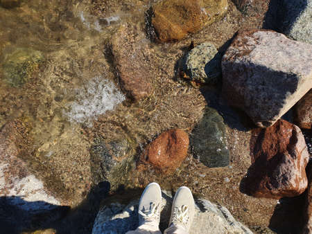 A man stands on a stone by the sea. Waves crash on the shore and rocks. One more step forward and you can get into the water.の写真素材
