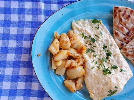 Delicious breakfast of scrambled eggs, potatoes and bread. The food is served on a blue plate.の写真素材