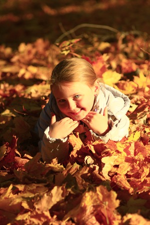little girl laying in yellow leaves in the autumn parkの写真素材
