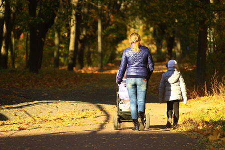 woman with baby in perambulator and elder child walking in the autumn parkの写真素材