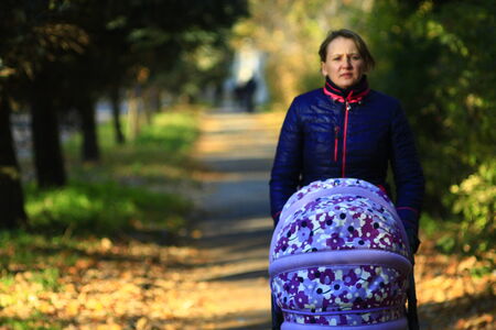 woman with baby in perambulator walking in the autumn park