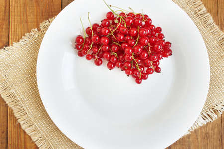 Berries of a red currant on the white plate on the brown wooden textureの写真素材
