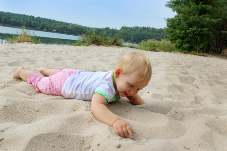 happy baby lays on the white sand at the riverの写真素材