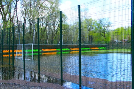 Football field during the flood of river. Small football stadium fenced with net is flooded with water during flood. Football has taken breakの写真素材