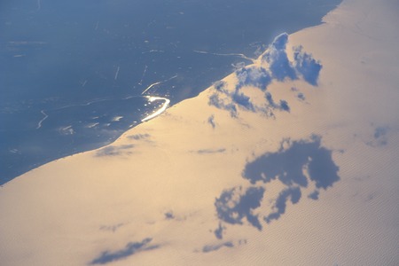 Beautiful view from window of plane flying over clouds and marine coastline. Clouds moving above water surface of sea. Landscape with view to Earth with river sea and clouds from aboveの写真素材