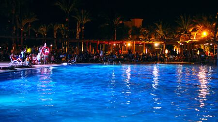 Holidays at Egyptian resort. People have a rest near pool in evening. Foreign tourists relax in evening near pool. Bright lights of resort hotel in Hurghada. Traveling conceptのeditorial素材