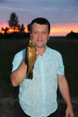 Man with big tench in hand. Fishing. Glad man with caught fish. Summer fishing