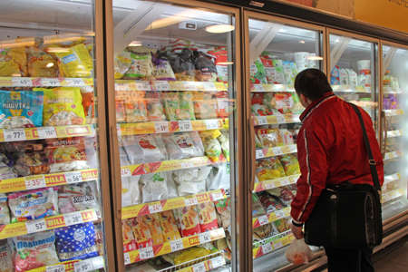 man choosing food in refrigerator of supermarket. Man is looking for frozen food in store. Man...