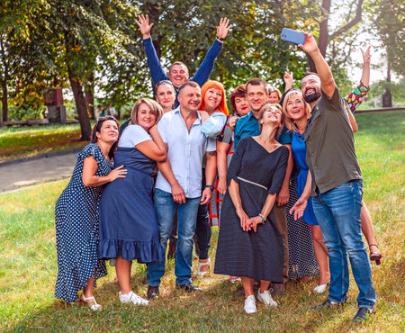 Meeting of classmates. Beautiful women and men glad to meet. Gathering of old friends. Cheerful company taking selfie. Group of young people making a photo on phone. Group portraitのeditorial素材