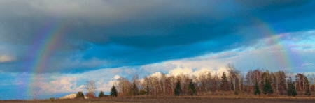 Bright rainbow in the sky with clouds above row of trees. natural landscape. natural landscape. Multicolored rainbow above poplars. Beautiful rainbow after rain. natural landscapeの写真素材