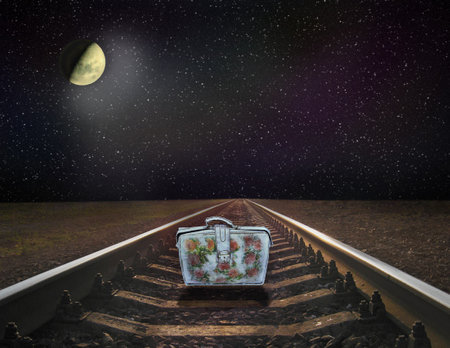 Night railway road. Rails with cosmic landscape. colorful suitcase standing on railway rails on nighty sky. Rails with cosmic landscape. lonely suitcase standing on rails.bright Moon shines from spaceの写真素材