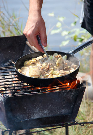 Cooking fried mussels in frying pan. Frying fresh mussels and onions near river. Cooking fresh caught mussels. Dish from fried fish cooked on fire. Pleasant rest by river. Summer holidayの写真素材