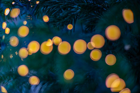 Warm golden bokeh lights glowing on evergreen branches creating a festive soft abstract holiday background.の写真素材