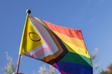 Progress Pride Flag featuring intersex symbol flying outdoors in sunlight against a clear blue sky. A vibrant symbol of inclusion, diversity, and LGBTQ rights.の写真素材