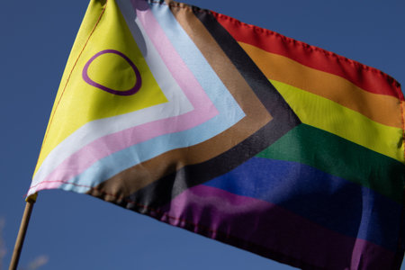 Progress Pride Flag with intersex circle waving in the wind against a clear blue sky. Symbol of LGBTQ pride, inclusion, and human rights.の写真素材