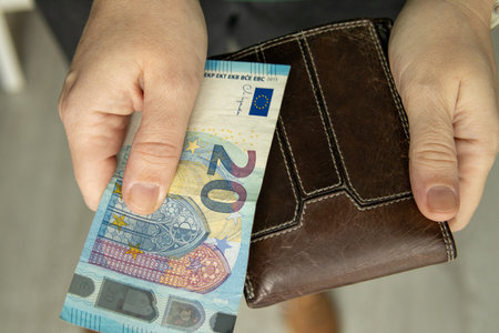 Hand holding a 20 euro banknote next to a leather wallet. Concept of personal finance, budgeting, cash payment and money management.の写真素材