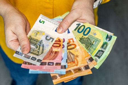 Hands holding a fan of colorful euro banknotes, symbolizing cash payment, savings, budgeting and financial planning.の写真素材