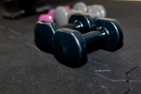 Small black dumbbells lying on gym floor mat, close up fitness equipment for home workout, strength training and healthy lifestyle concept.の写真素材
