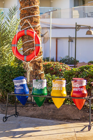 Colorful recycling bins for plastic, paper, glass and metal outdoors near palm tree. Waste sorting...