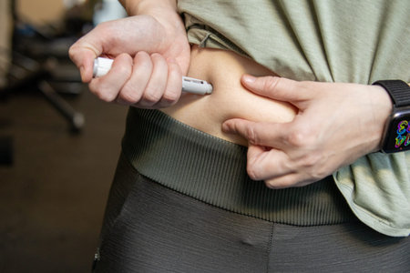 Close-up of an adult woman self-administering a weight management injection into the abdomen at home.の写真素材