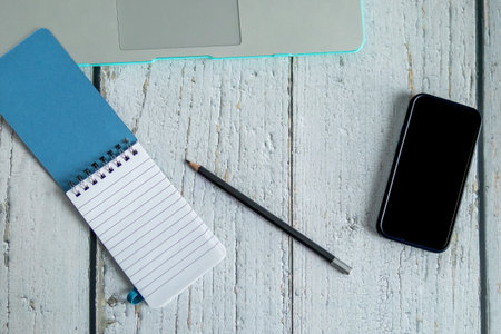 Flat lay workspace with laptop edge, smartphone, spiral notebook and pencil on rustic wooden table. Remote work, planning and productivity concept with copy space.の写真素材