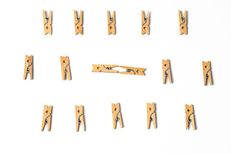 Wooden clothespins arranged in structured rows on white background with two pegs placed horizontally in the center. Minimal geometric flat lay with strong natural shadows and creative composition.の写真素材