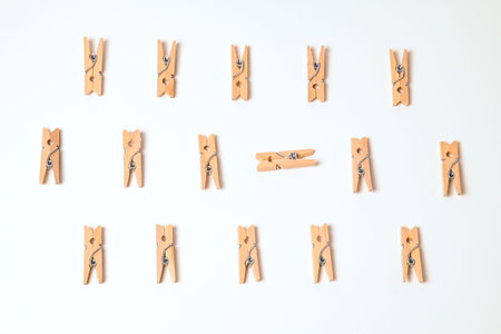 Wooden clothespins arranged in a regular grid on white background, with one peg placed horizontally in the center breaking the pattern. Minimal flat lay with strong natural shadows and clean composition.の写真素材