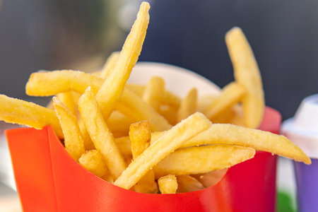 Close-up of golden crispy french fries in a red takeaway container. Fast food snack served in a...