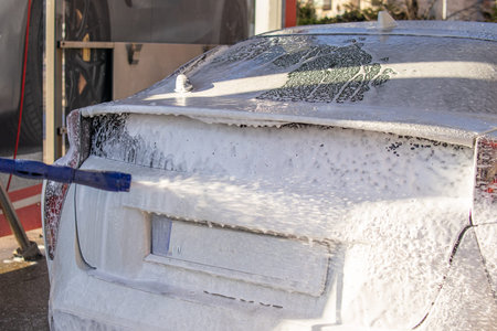 Rear view of a car covered with foam during washing at a self service car wash. Cleaning vehicle with high pressure water.の写真素材