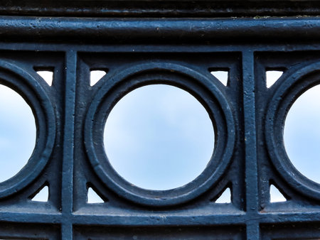 Close-up of geometric metal structure with repeating circular elements and cloudy sky in background. Industrial abstract pattern with symmetry and minimal design