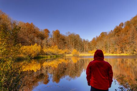 Hiker overlooking a small mountain lake while in the autumn forestの写真素材