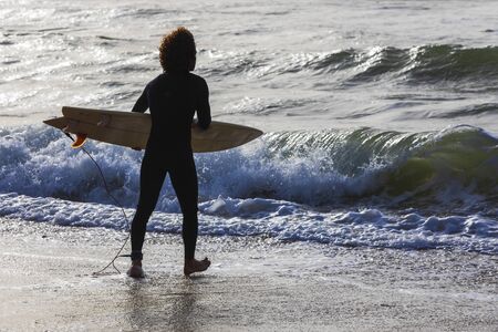 A surfer with a board enters the water