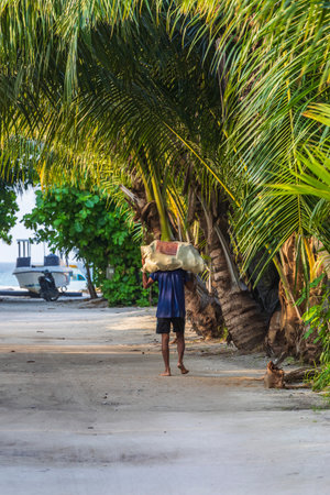 Thoddoo, Maldives - February 05, 2025: A local resident carrying a heavy bag on his shouldersの写真素材