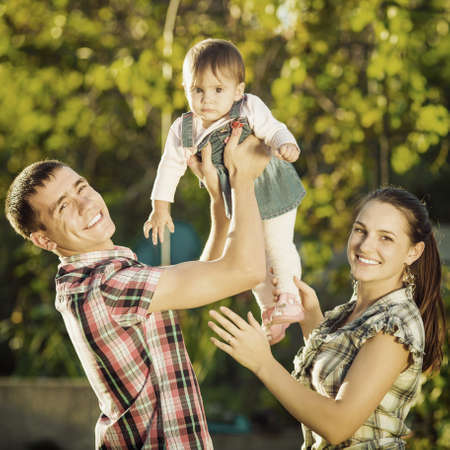 Happy young family having fun outdoors in summer. Mother, father and their cute baby-girl are...