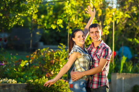 Young couple in love is having fun outdoors. Young beautifull man and woman dressed in casual country style are hugging in a sunny garden. Tender relationship concept. の写真素材