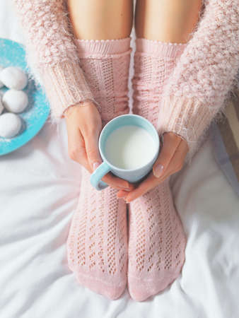 Woman relaxing at cozy home atmosphere on the bed. Young woman with cup of milk in hands and cookies...