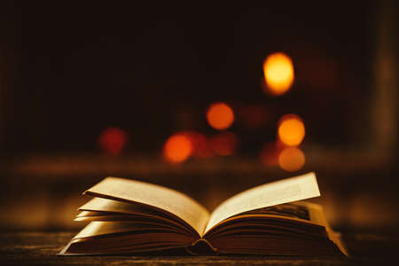 Open book by the Fireplace with Christmas ornaments. Open storybook lying on a wooden bench by the fireside. Cozy relaxed magical atmosphere in a chalet house decorated for Christmas. Holiday concept.の写真素材