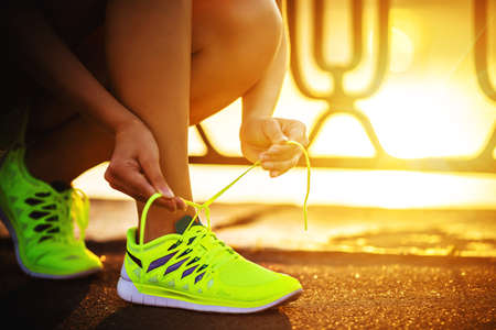 Running shoes. Barefoot running shoes closeup. Female athlete tying laces for jogging on road in...