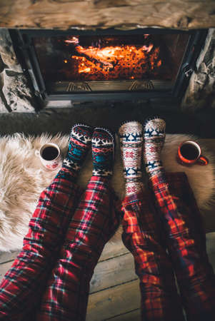 Couple sitting under the blanket, relaxes by warm fire and warming up their feet in woolen socks.の写真素材