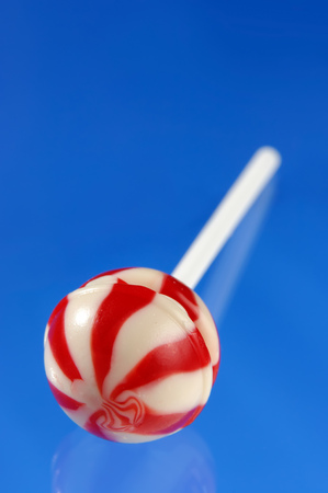 Colorful red white stripy lollipop isolated on blue backgroundの写真素材