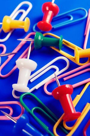 Colorful thumbtacks and paperclips on blue background, office supplies conceptual still lifeの写真素材