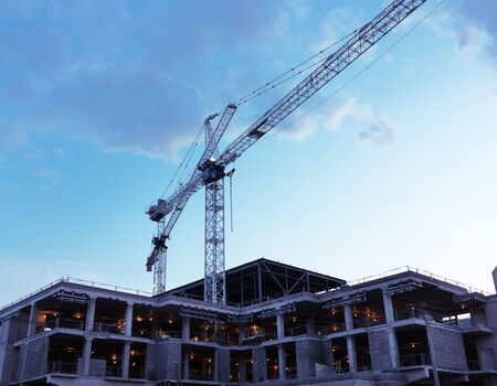 Artistic photo of a crane at a construction site at sunset over blue skyの写真素材