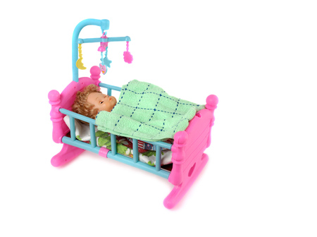 Baby doll in toy bed isolated on white background