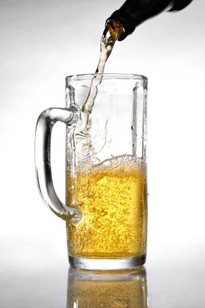 Light beer pouring from a bottle into a tall beer glass Artistic food still life over white backgroundの写真素材
