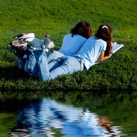 Two girls on grass near water studying in the natureの写真素材