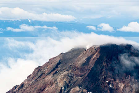 An aerial view of an Alaskan peak surrounded by smoky clouds and a blue sky. Scenic mountain in...