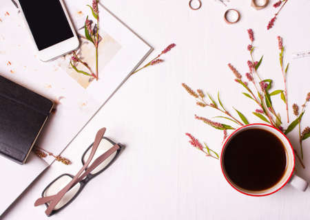 Top view of designer table, a woman with a cup of coffee, magazine, phone, glasses, rings, flowers...