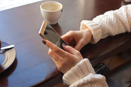 girl, woman holding a mobile phone in hand, sitting in a cafe